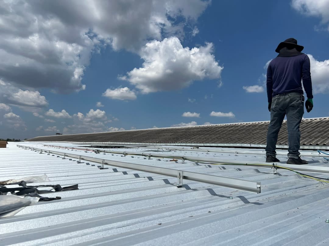 Crew installing solar panel mounting rails on a metal-sheet warehouse roof in Natai, Phang Nga